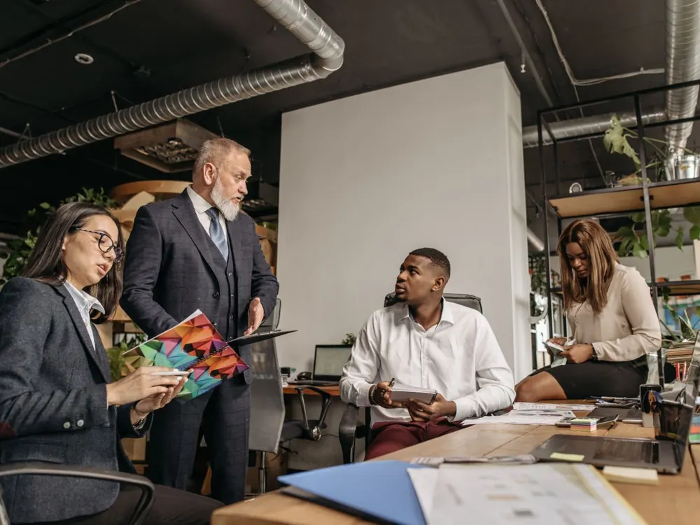 Colleagues in business clothes meeting around desks in an open-plan office