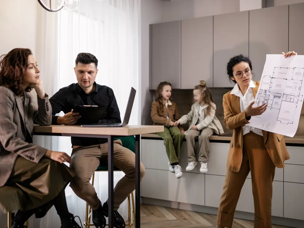 A real estate agent holding up a floor plan for a family seated in a modern kitchen