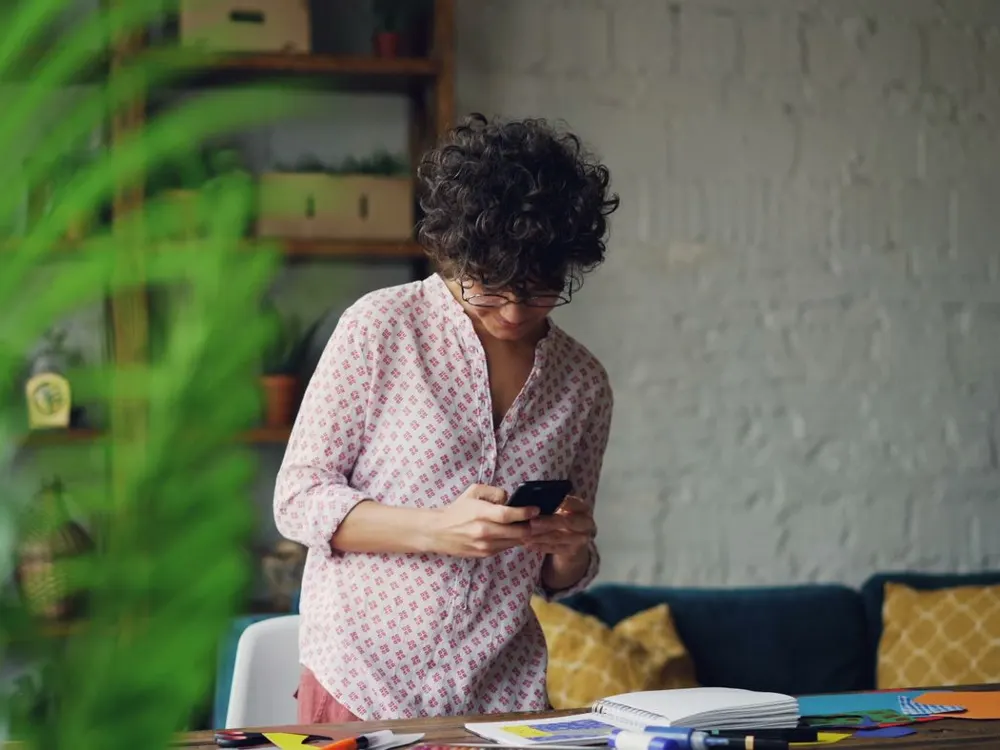 A woman standing in a home office looking at her smartphone