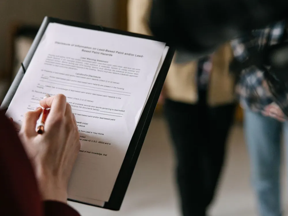 A close-up of a person signing a printed document on a clipboard